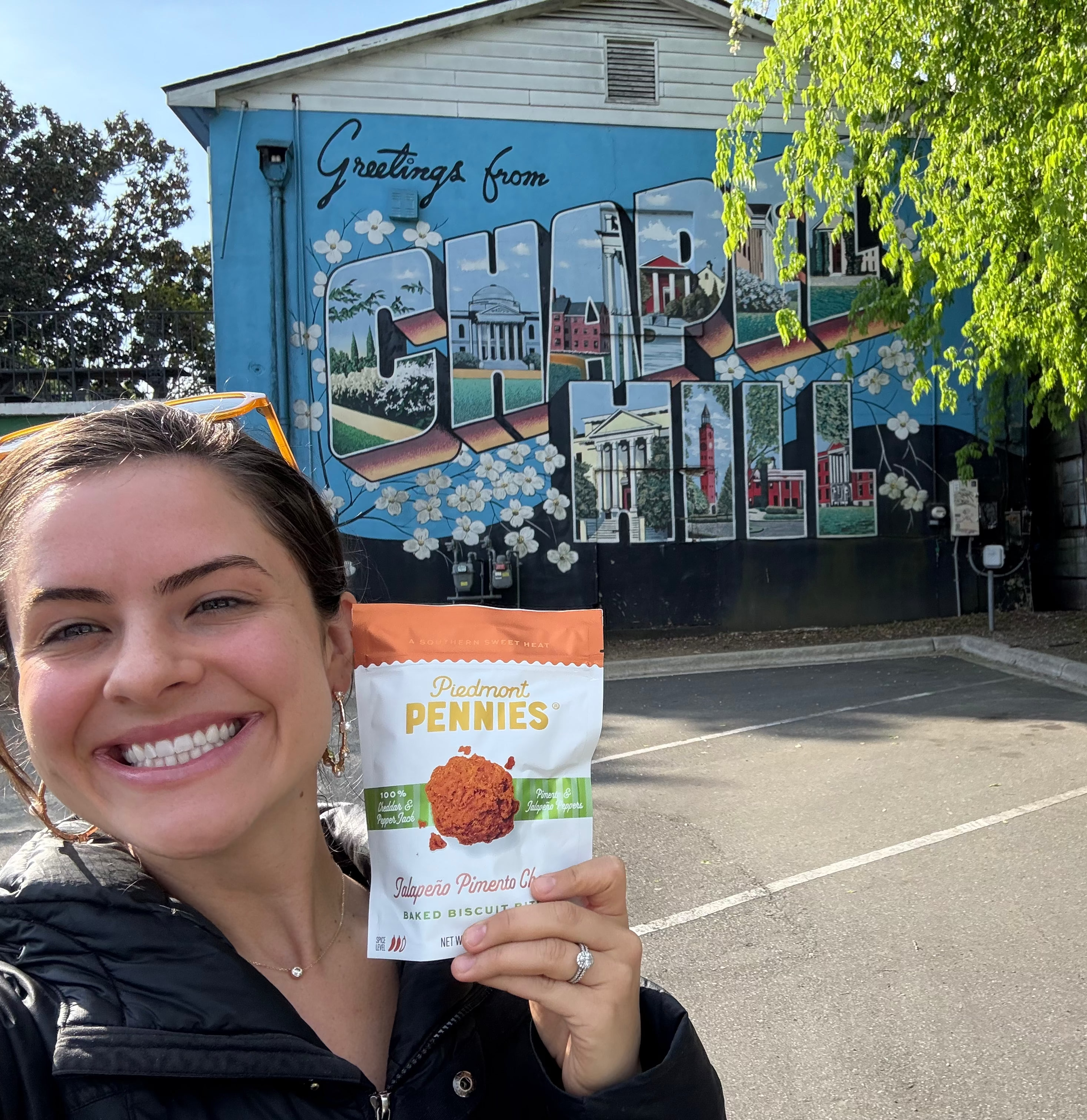 Woman holding a piedmont pennies product package in front of a colorful mural on a building.