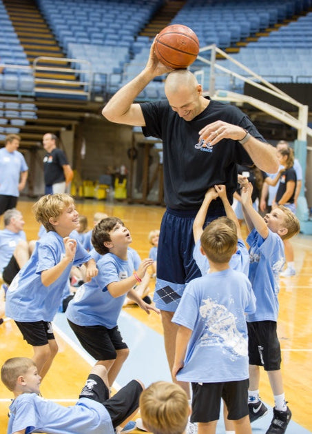 Coach demonstrating basketball skills to a group of children on a basketball court.